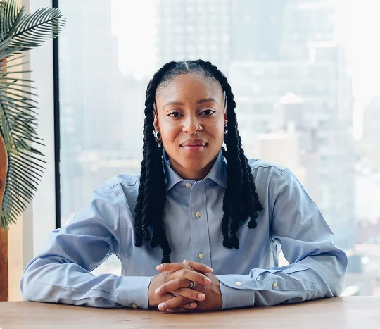 Octavia Carson, a woman with dreadlocks, sits at a table with a panoramic view of the city in the background