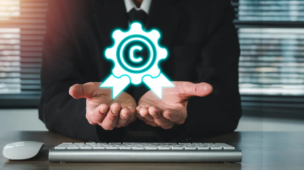 Person in formal attire holding glowing copyright symbol above keyboard and mouse on desk.