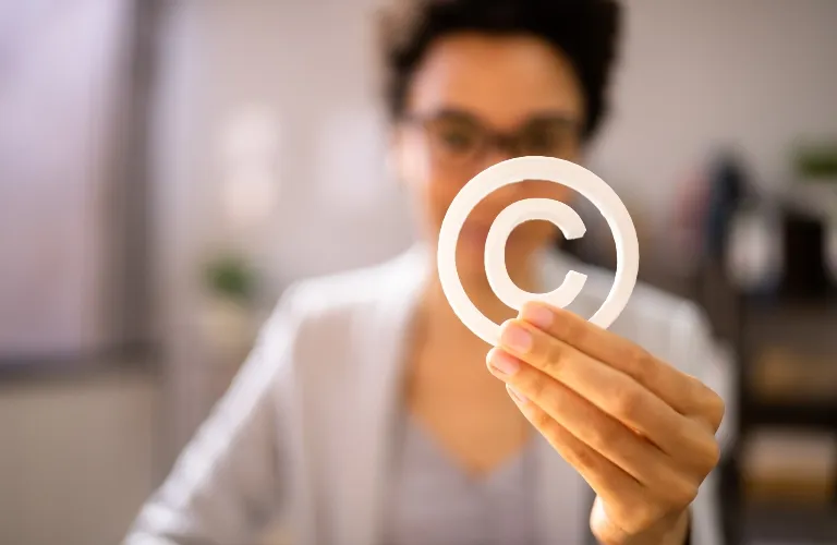 Person holding a white copyright symbol with blurred office background.