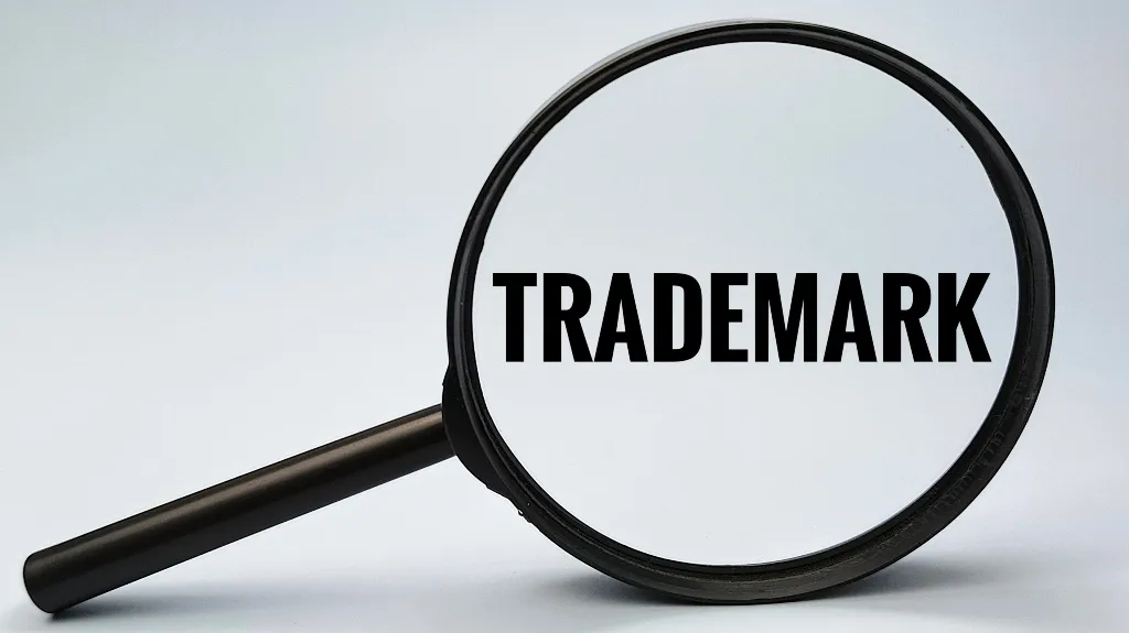 Magnifying glass enlarging the word "TRADEMARK" on a light background.